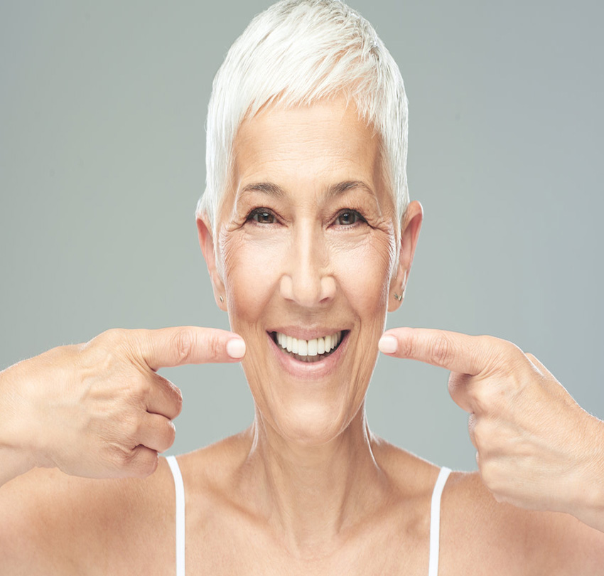 Beautiful Caucasian smiling senior woman with short grey hair pointing at her teeth and looking at camera. Beauty photography_