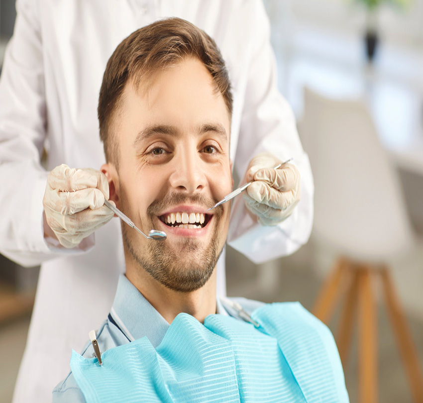 Portrait of male patient looking cheerful at camera in modern dentistry clinic during medical check up in medical center. Dentist examining young man teeth with dental tools. Dental health care_