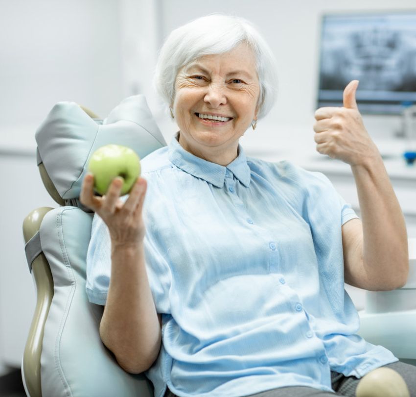 A woman sitting in a dental chair holding an apple, during a dental implant placement in Boulder, CO.