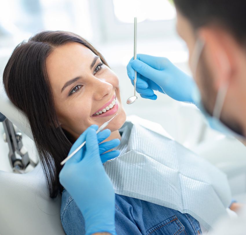 A woman smiles while seated in a dentist's chair, participating in dental hygiene education in Boulder, CO.